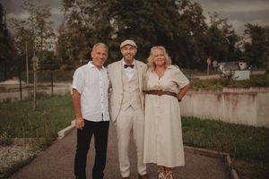 Three people in formal attire pose together outside Le Waldeck building.