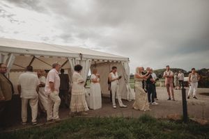 Wedding celebration under a white tent with guests in light colored formal attire.