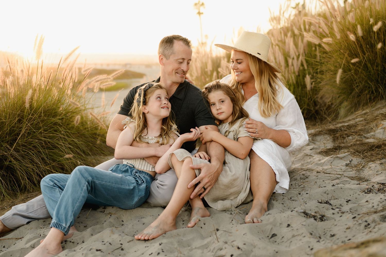 A family with two children enjoying time together on a sandy beach at sunset.