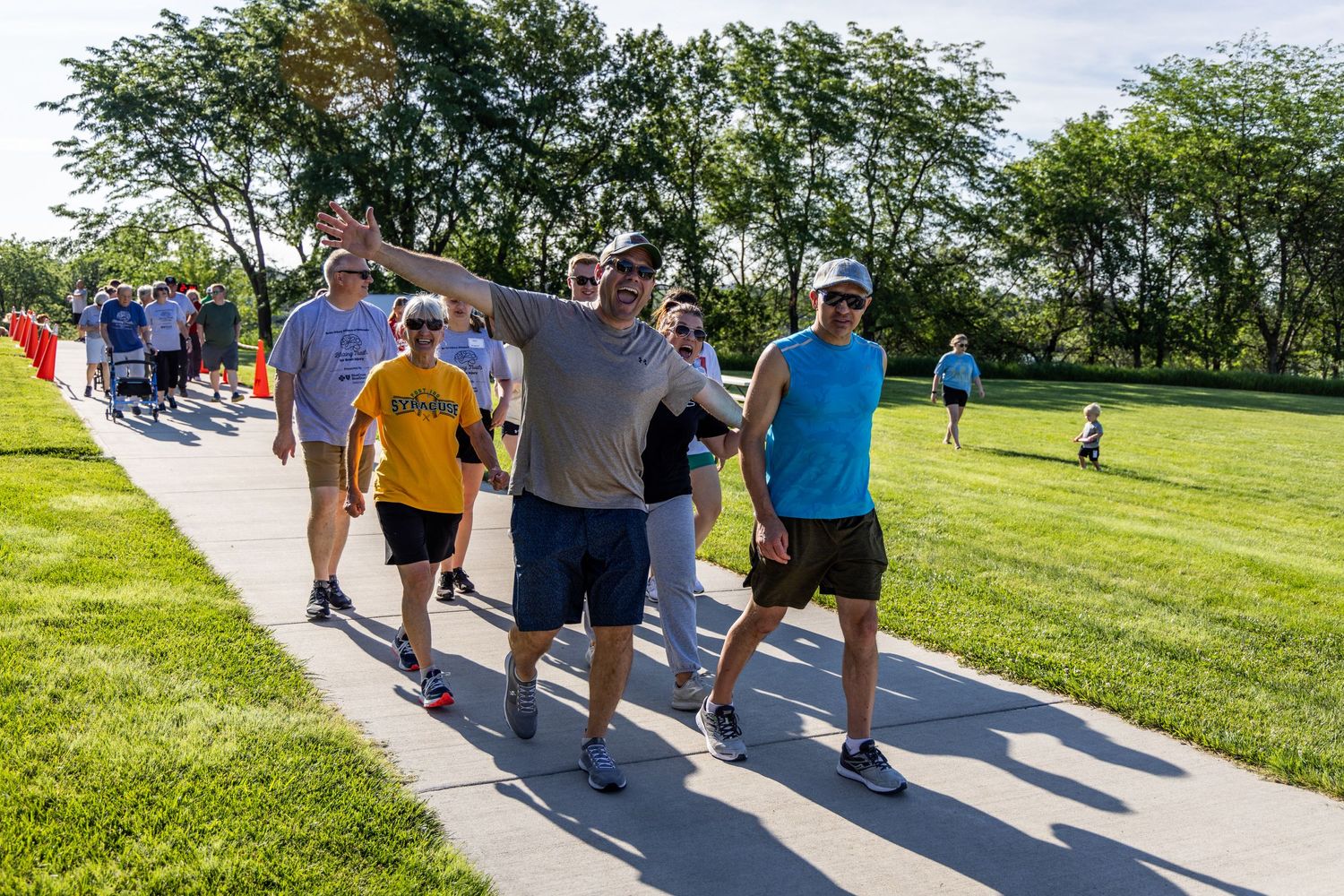 Group of people walking together on a sunny path through a green park setting.