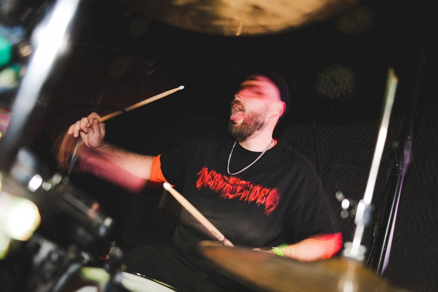 Drummer performing on stage with red lighting effects.