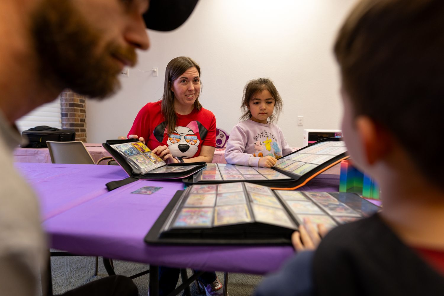 A group of people, including two women and a child, are sitting around a table and using electronic devices.