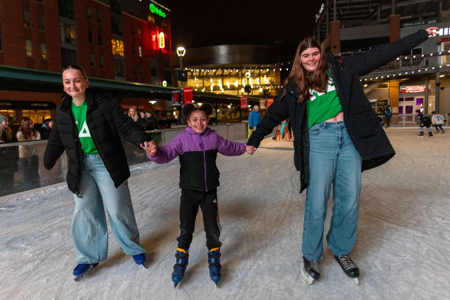 A group of people ice skating together on a public ice rink at night.