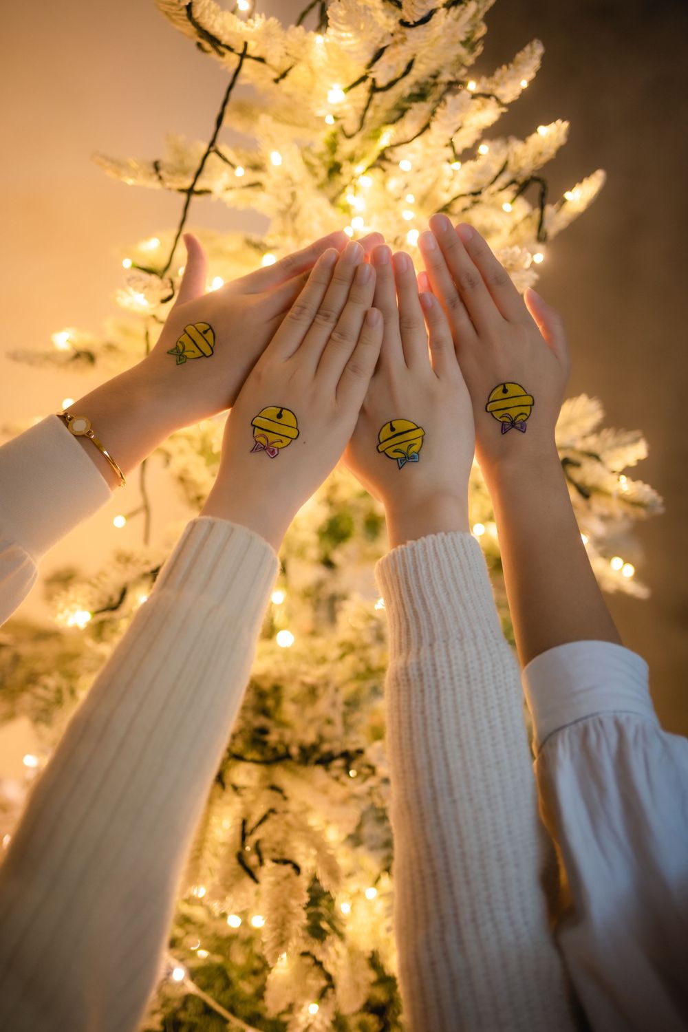 Hands with matching tattoos raised together against a glowing background with fairy lights.