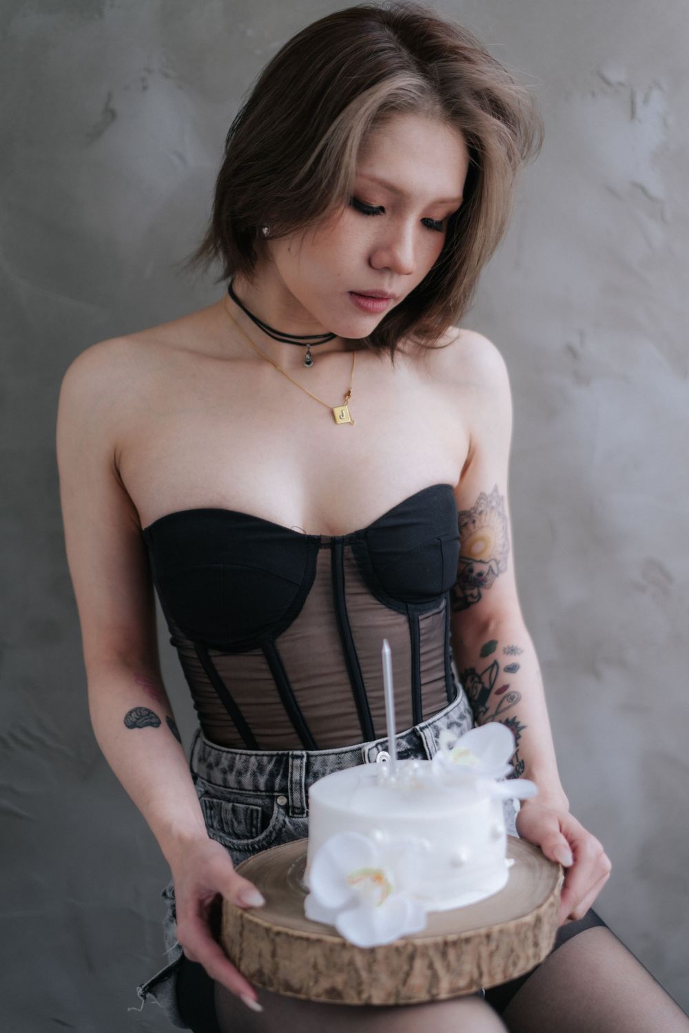 Person in black corset top poses with white cake on rustic wooden platter.