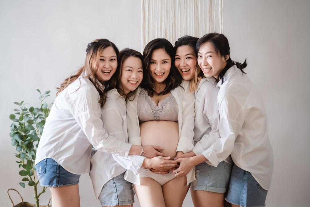 Friends in white shirts gather around expectant mother for maternity photo.