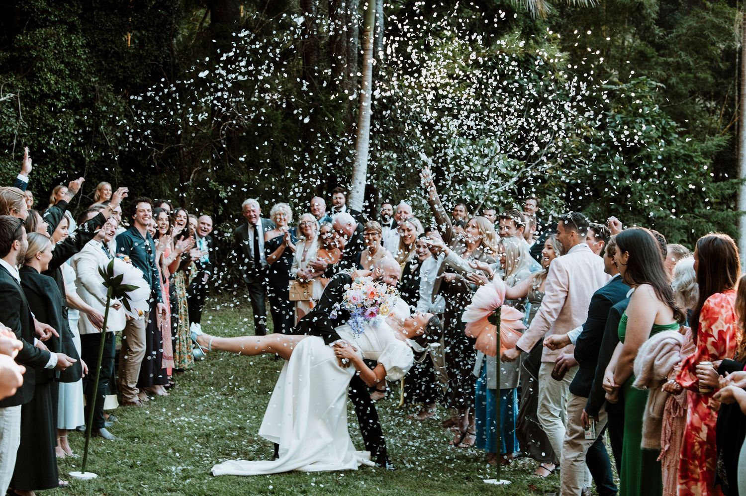 Wedding ceremony guests throwing flower petals in a garden setting.