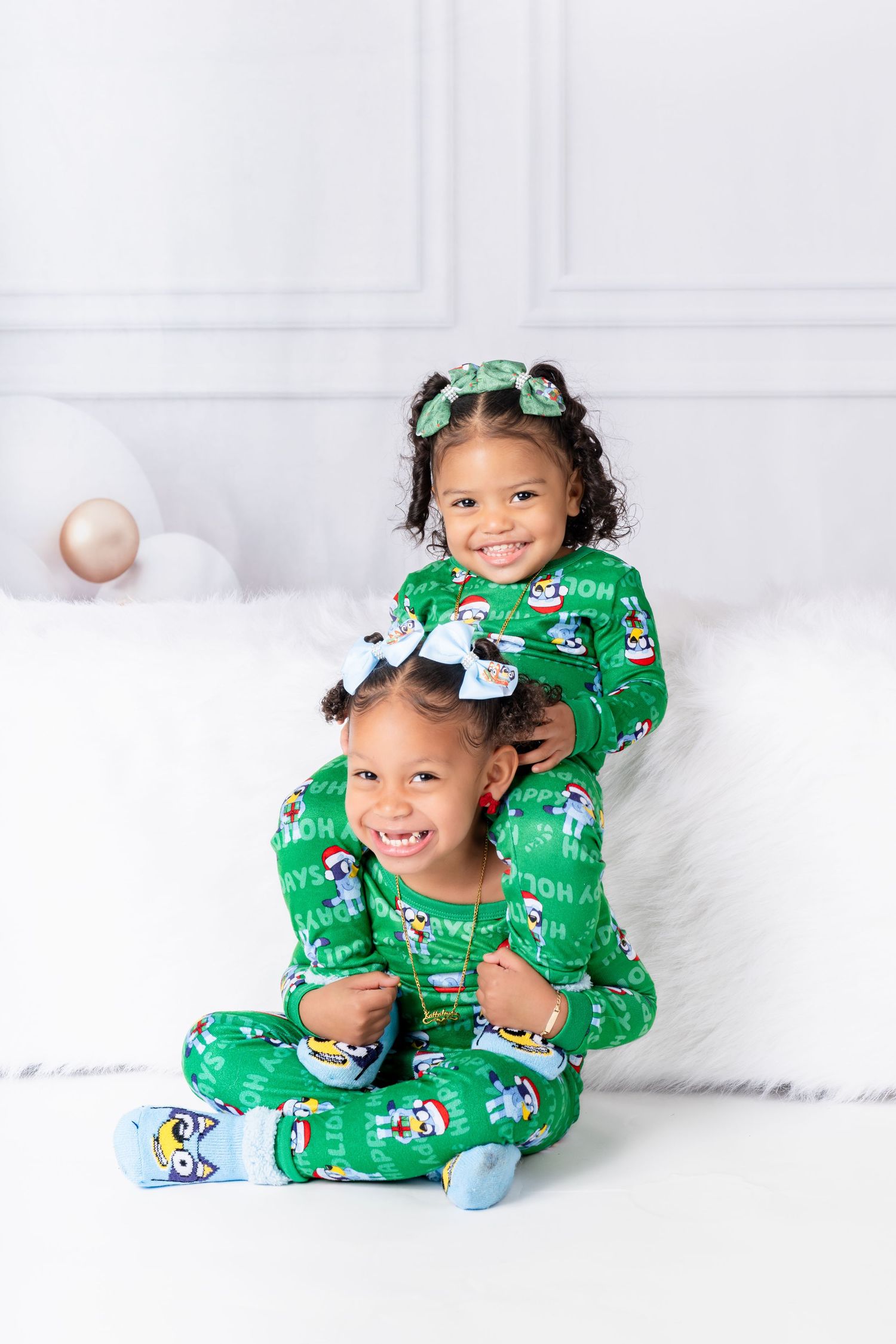 Two children wearing matching green holiday pajamas pose on white bedding.
