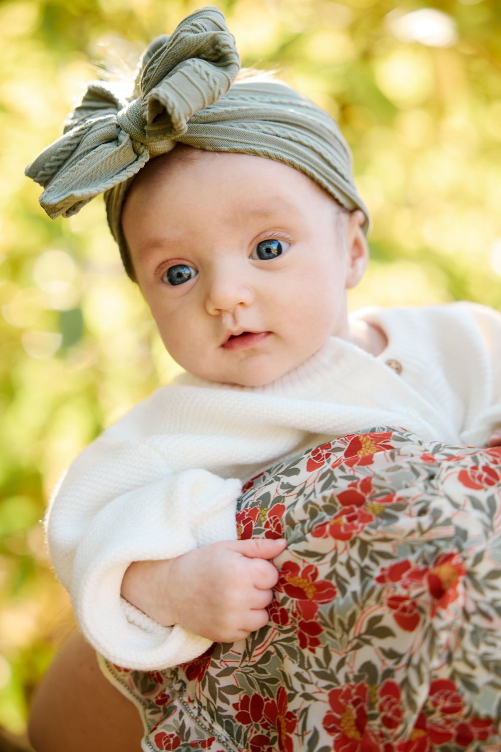 Baby wearing floral dress and beige hat poses against blurred golden background in series of close-up portraits.