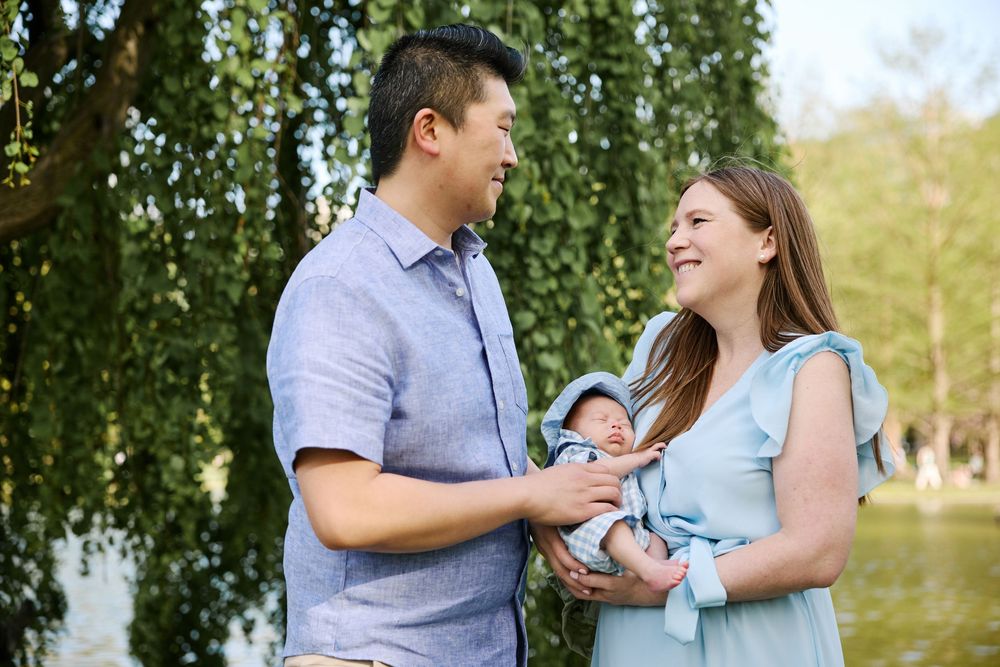 Couple in light blue and gray outfits share romantic moments during an outdoor photoshoot in a park setting.
