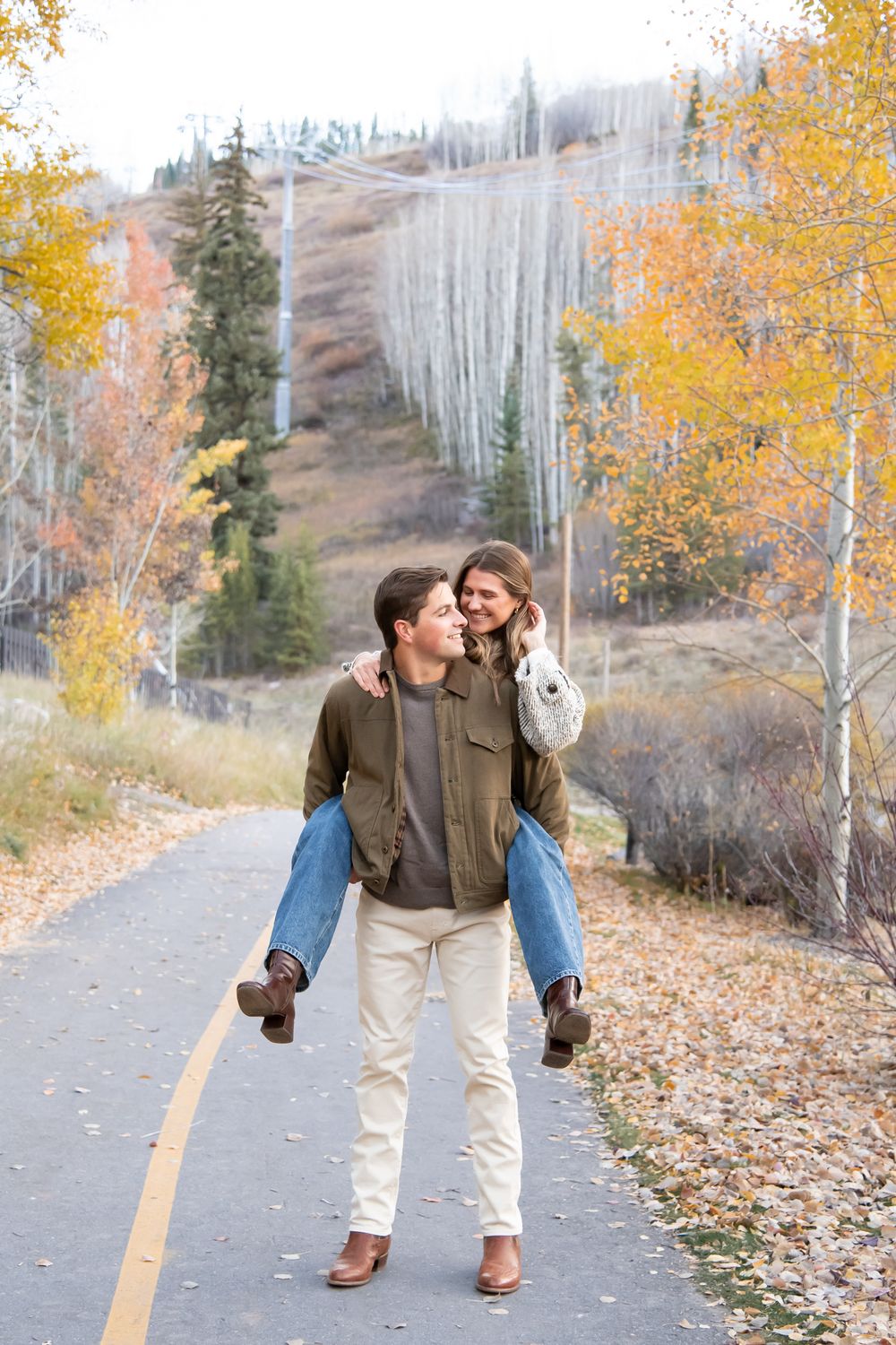 Candid and playful moment on an autumn path lined with golden aspen trees and mountain slopes with fashionable couple for Vail engagement