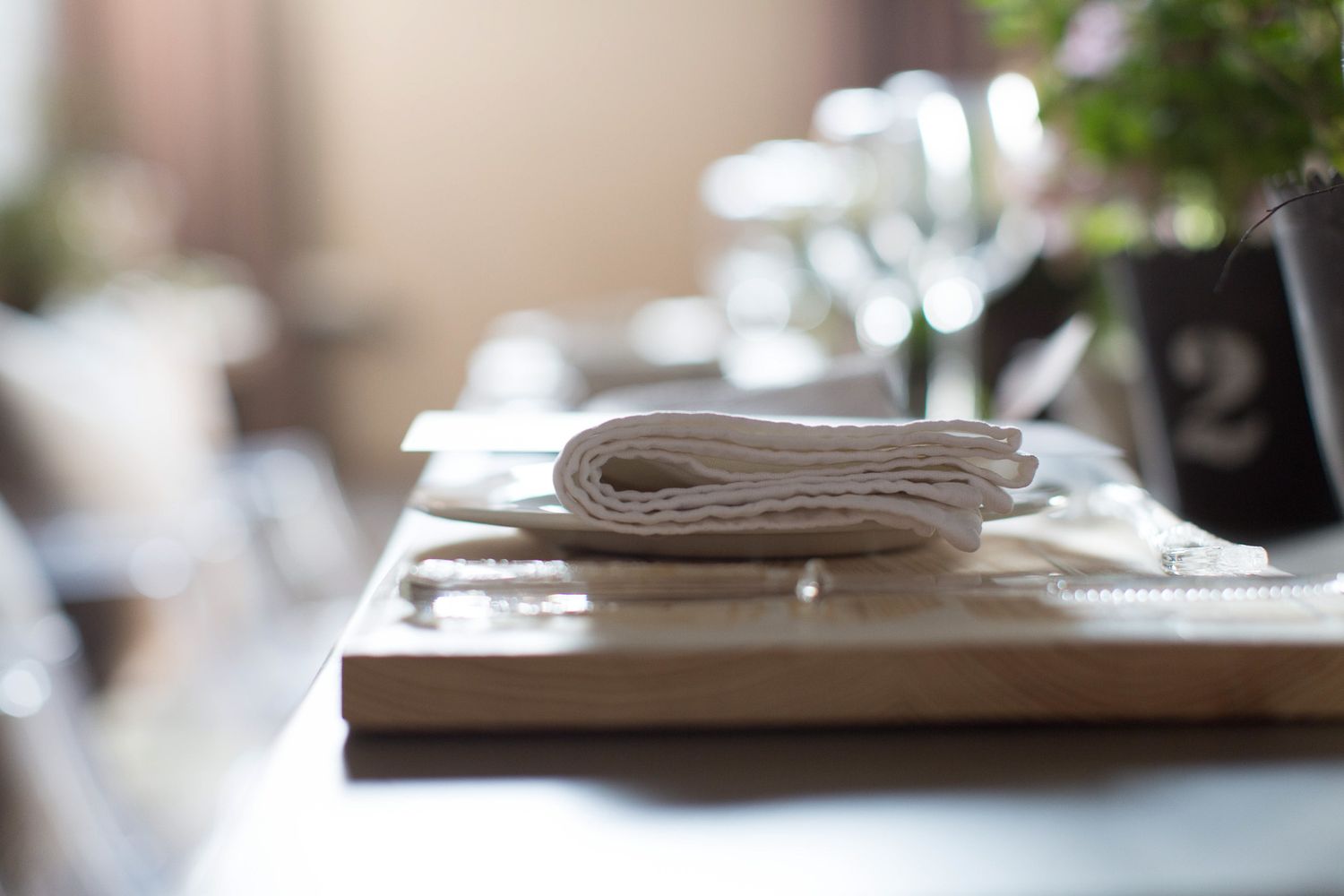 Close-up of a neatly folded white linen napkin on a wooden board at a restaurant table setting.