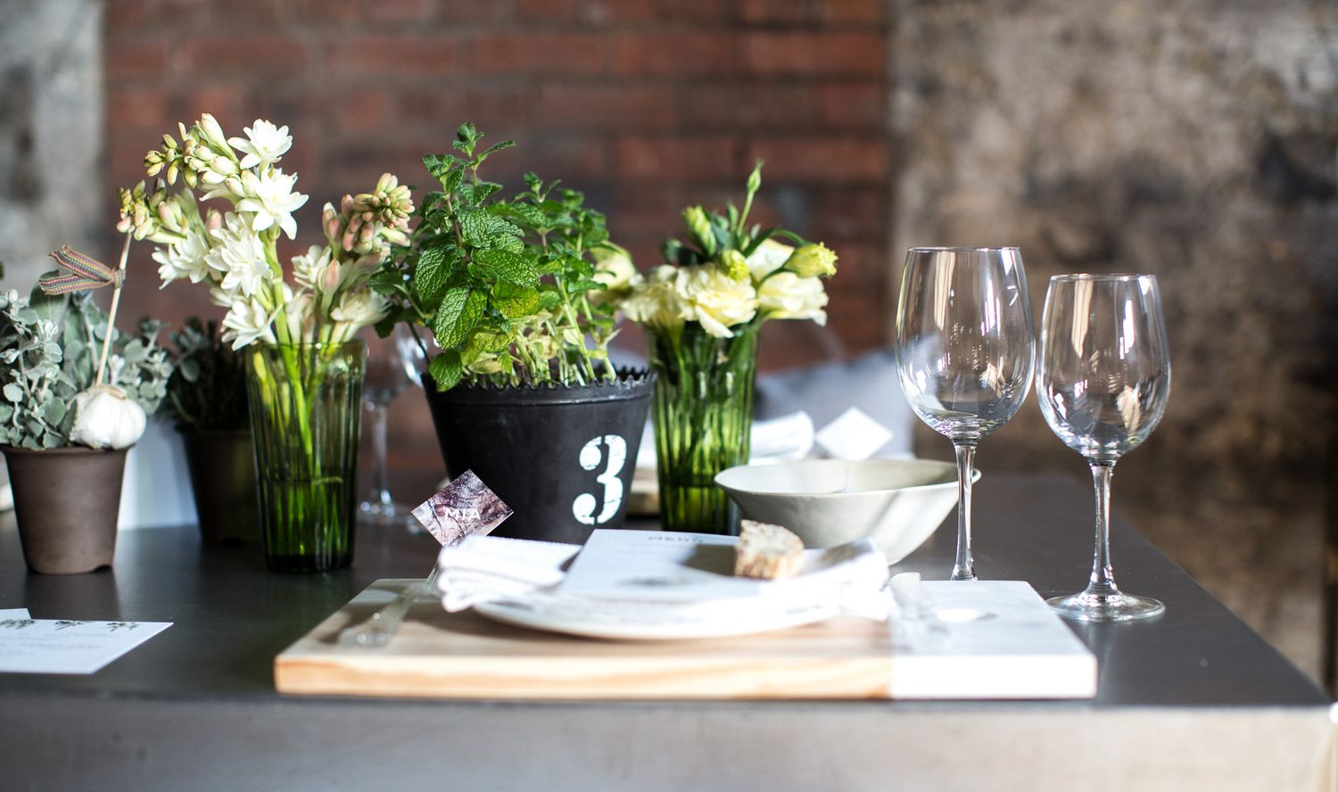 Rustic wedding table display featuring potted herbs, white blooms, wine glasses, and a chalkboard number 3 centerpiece.