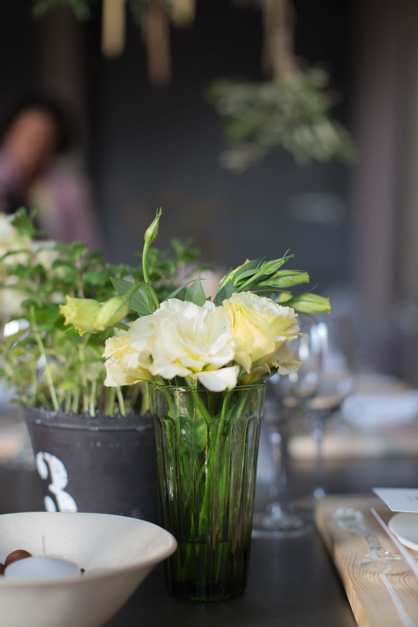 Close-up of white lisianthus flowers in a green glass vase on an elegantly styled dining table.