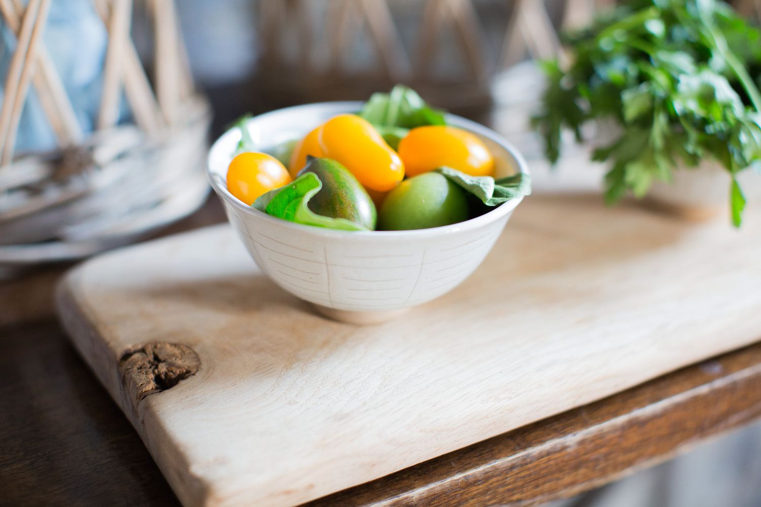 Fresh yellow and green cherry tomatoes in a white bowl on a rustic wooden cutting board.
