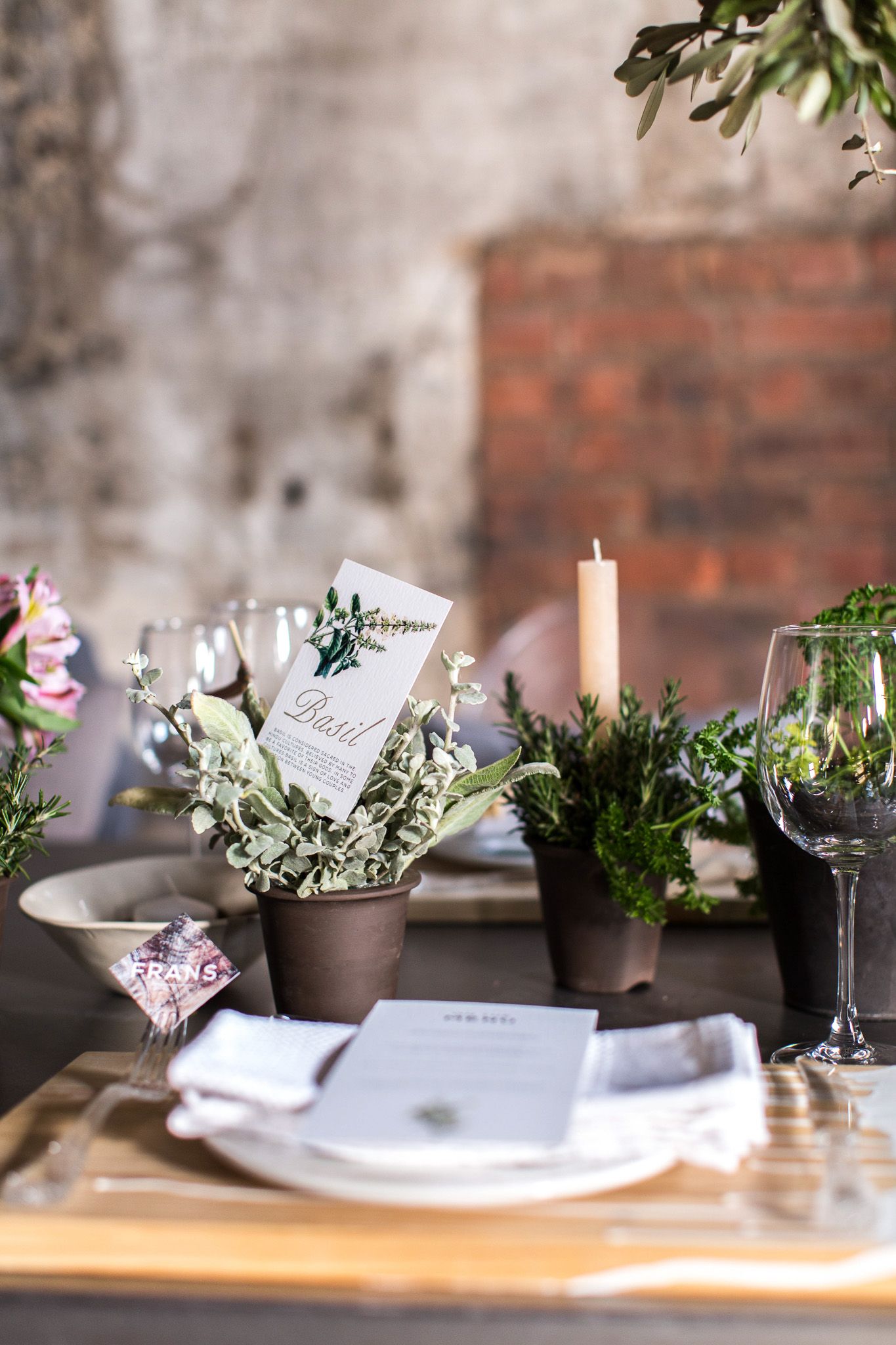 Rustic wedding table setting with potted herbs, candles, wine glasses, and elegant place settings on a wooden table.