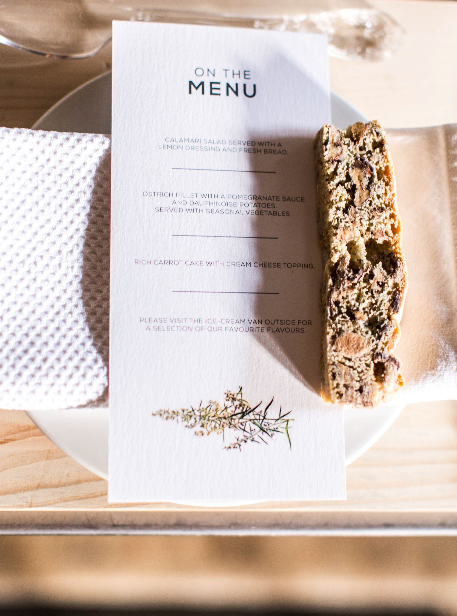 Elegant wedding menu card reading On The Menu displayed on a white plate with a slice of carrot cake.