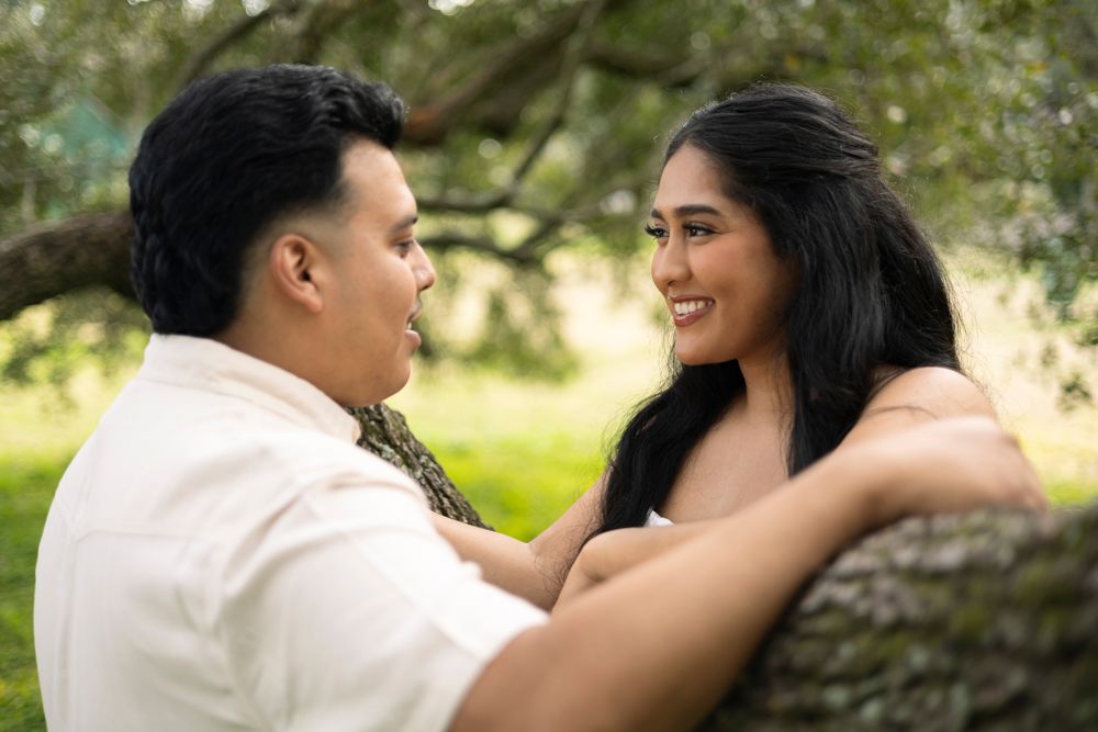 A couple sharing an intimate moment together outdoors with greenery in the background.