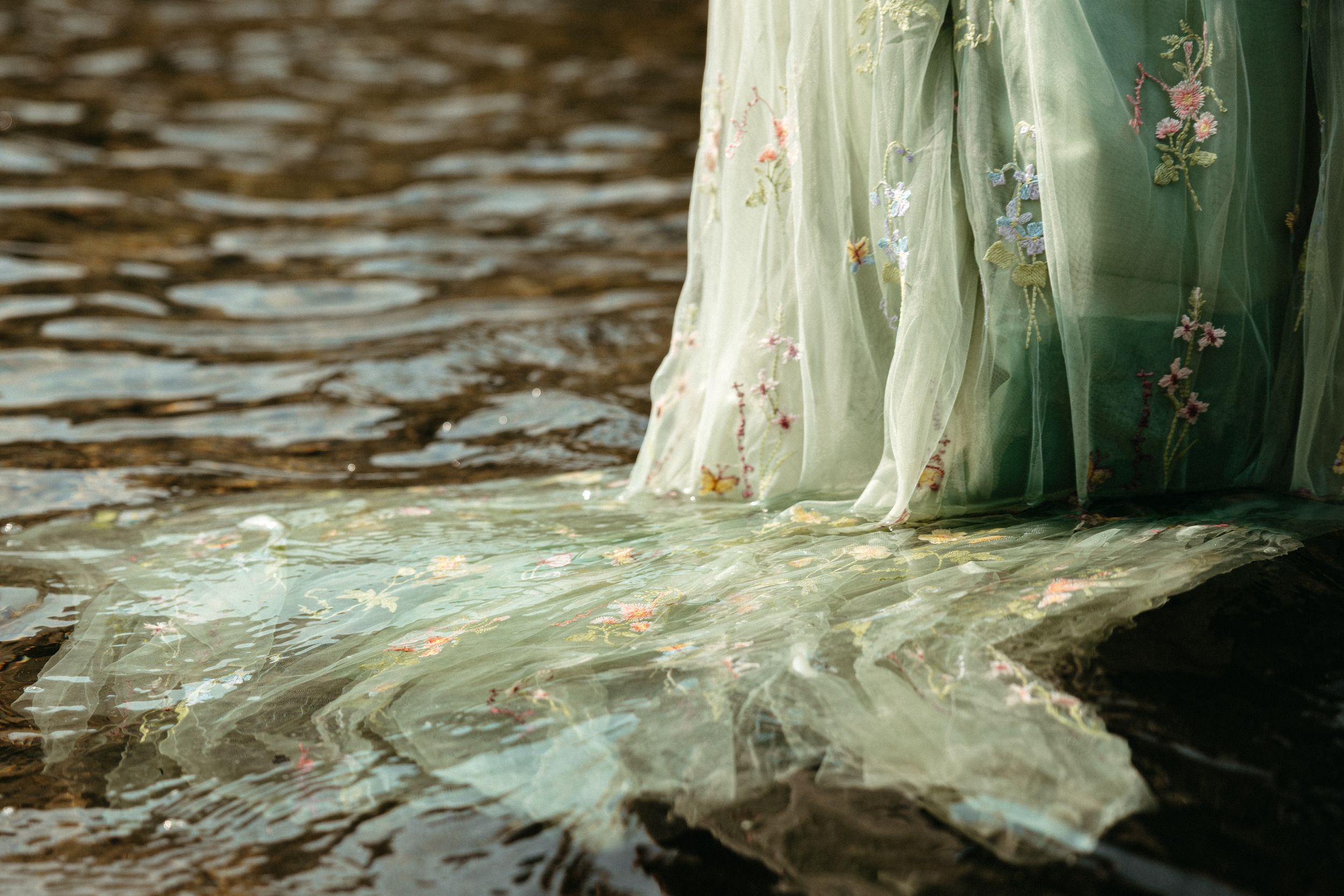 Delicate floral embroidered green tulle gown trailing gracefully in shimmering water.