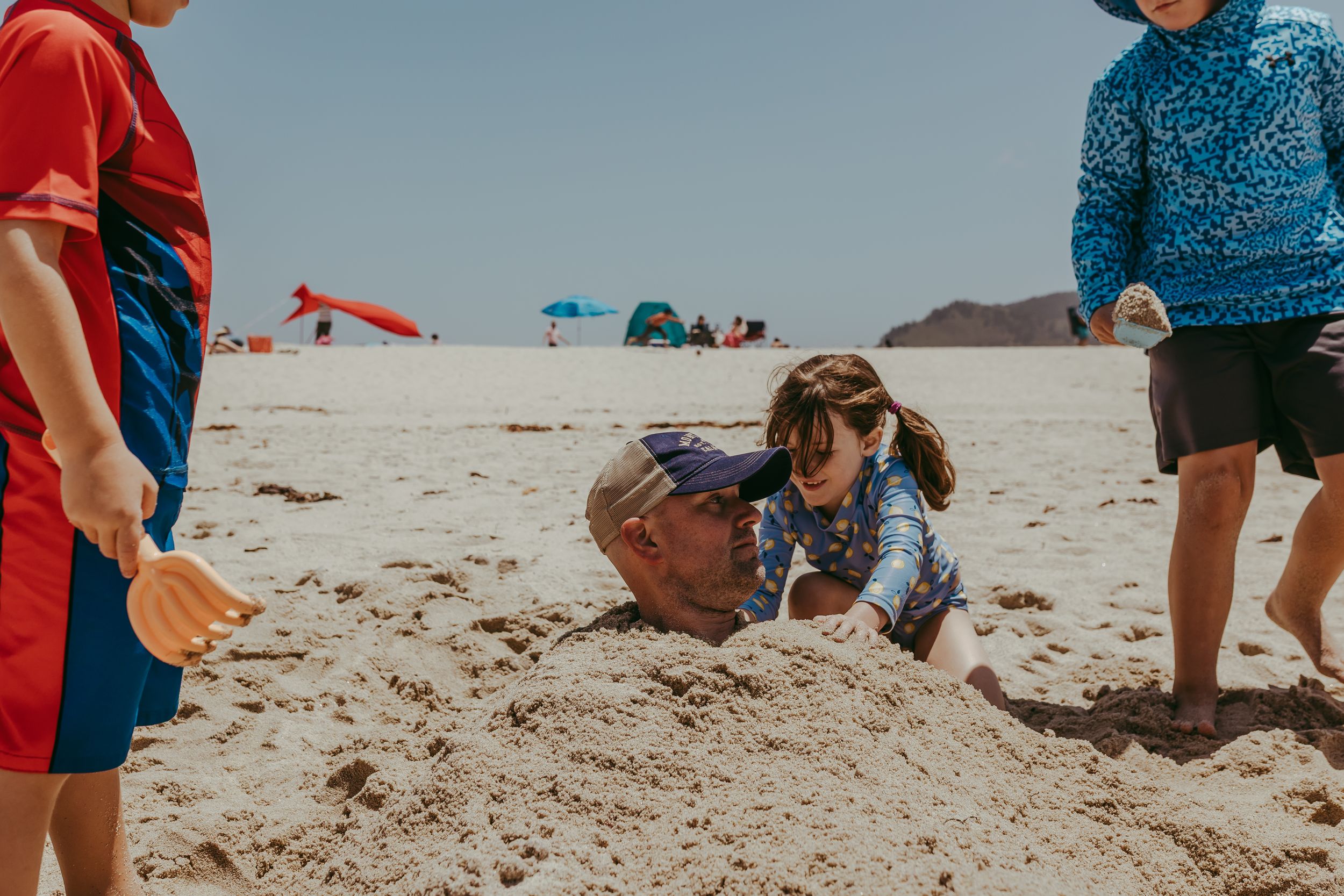 A group of children bury dad in the sand at the beach.