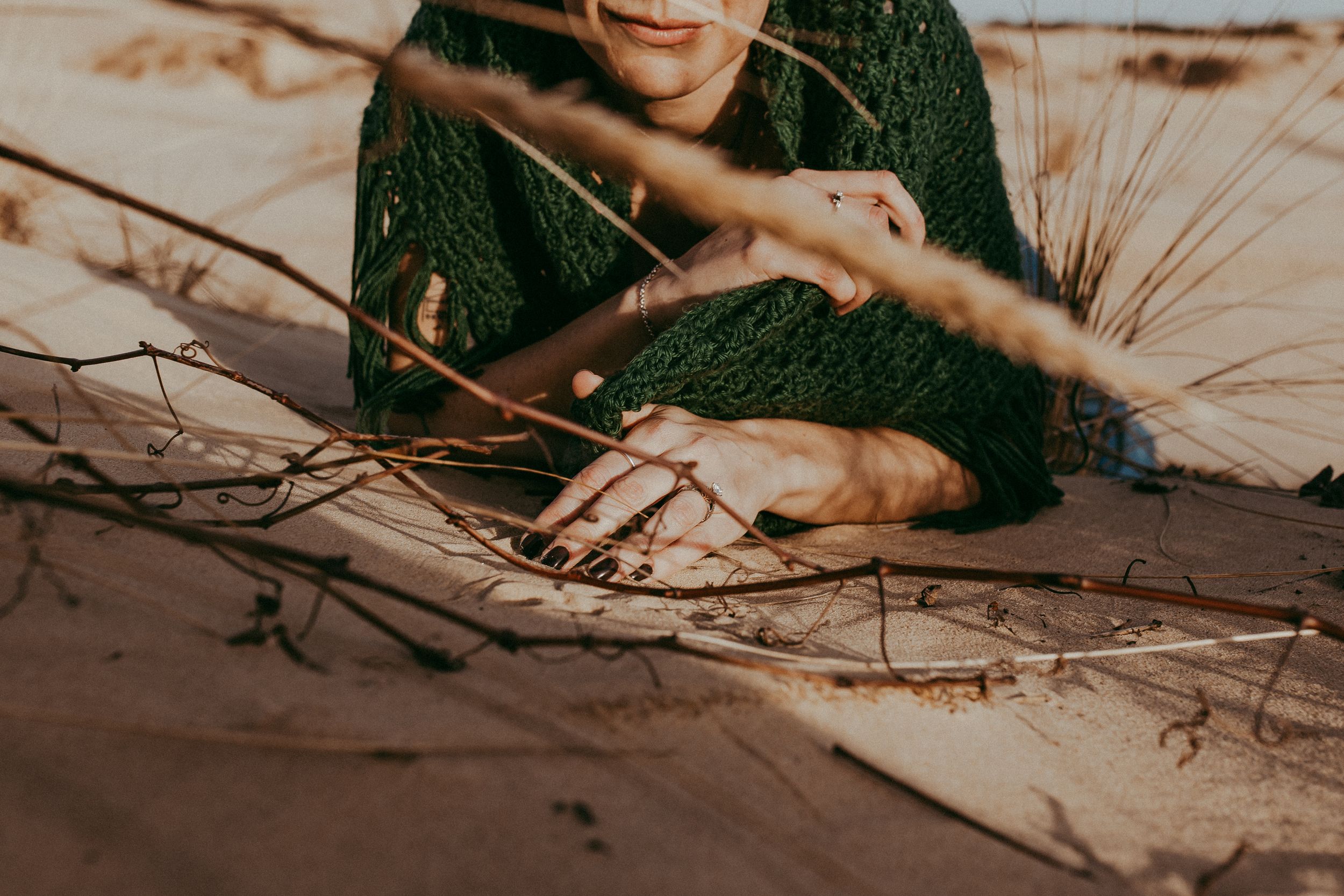 Woman wrapped in hand knitted shawl smiling while touching sand. Whitney Popp, Phoenix Arizona photographer.