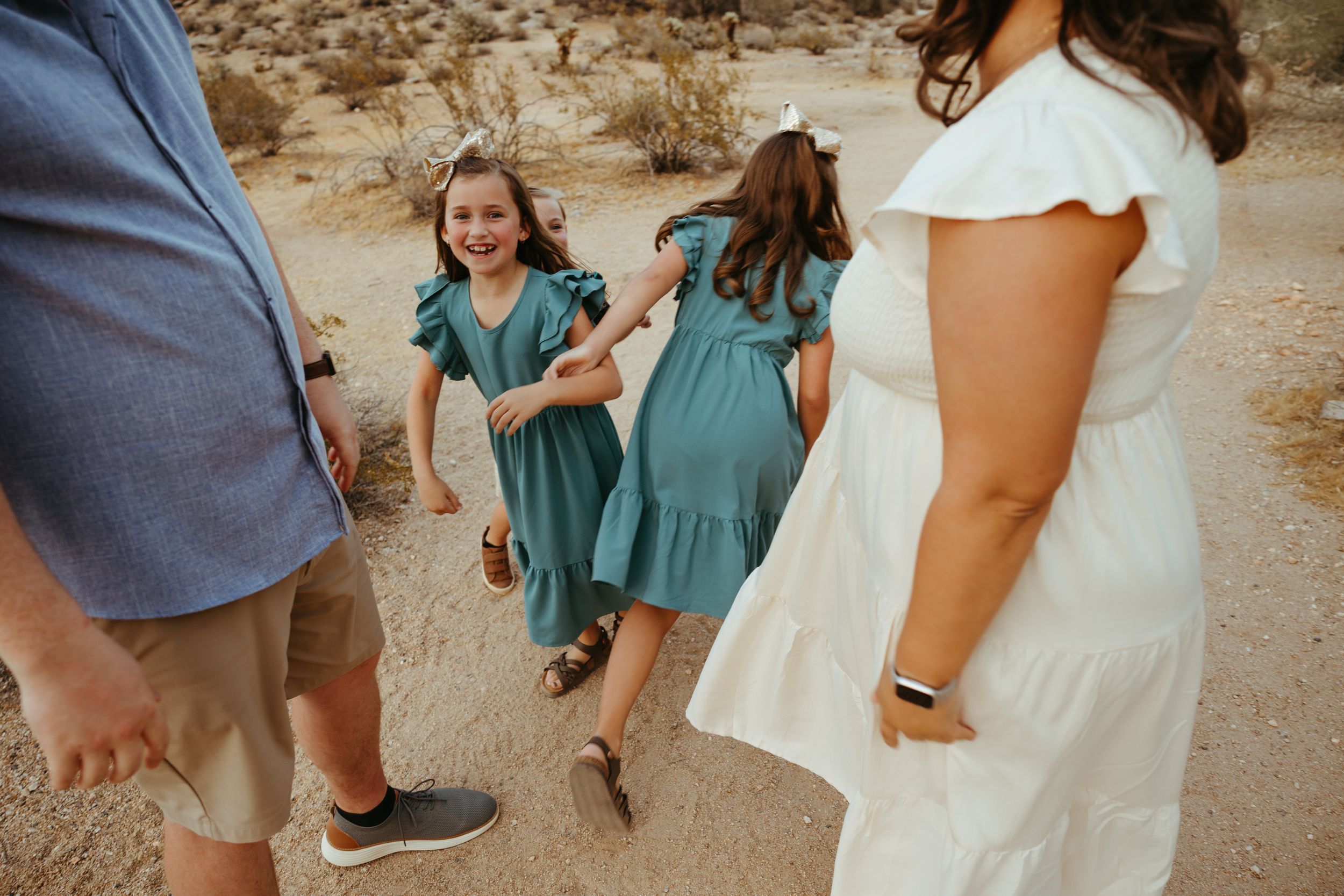 Two girls in matching teal dresses laugh and play together during a desert family photo session.