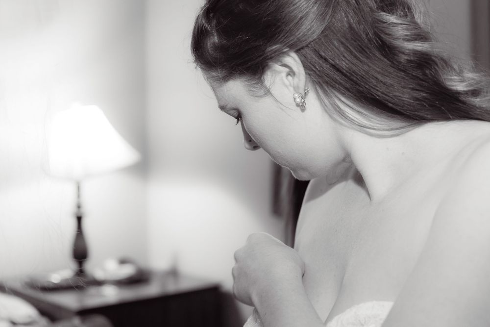A candid black and white photograph captures a bride getting ready on her wedding day, focusing on final preparations.