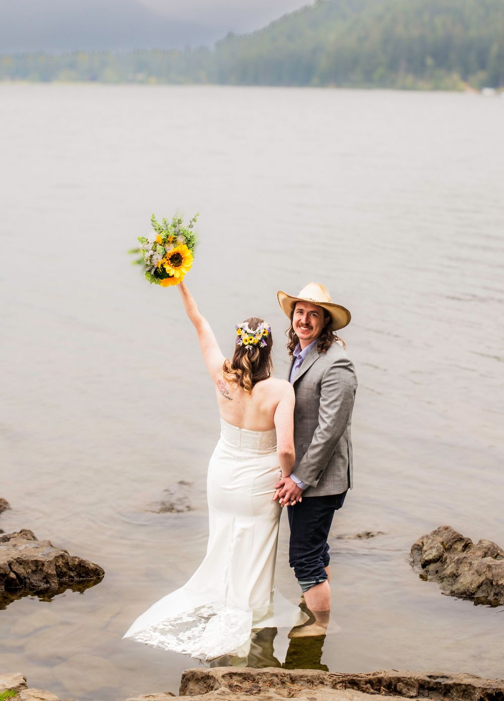 A joyful couple celebrates their wedding by the scenic lakeside, surrounded by rocky shores and distant hills.