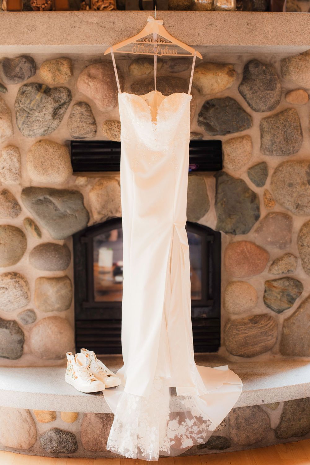 White lace wedding dress hangs elegantly against rustic stone wall in natural light.