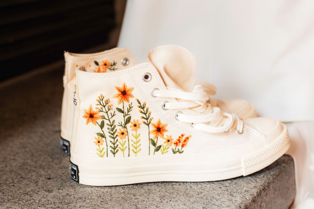 White canvas high top sneakers with delicate orange and yellow floral embroidery detail on the sides.