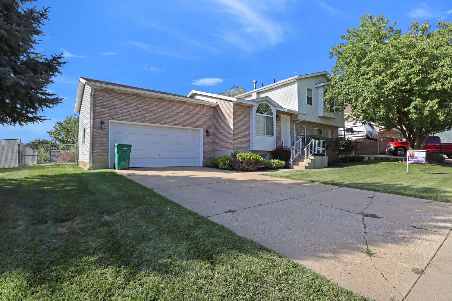 Bi-level brick suburban home with white garage door, mature trees, and well-maintained green lawn on quiet street.