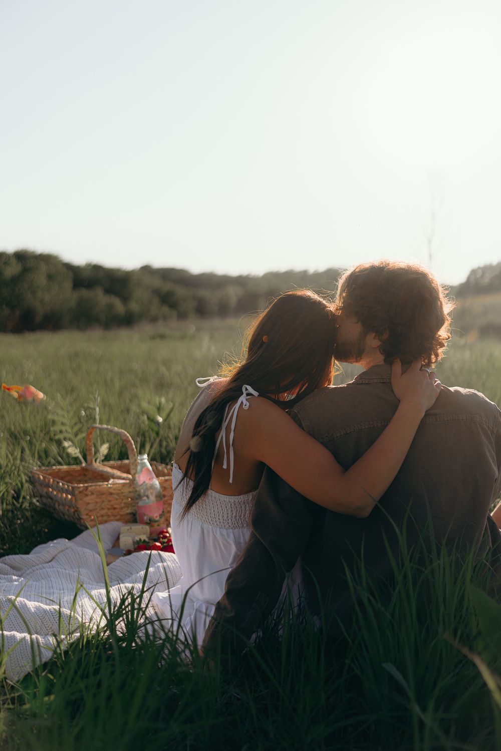 Romantic couple embracing during sunset picnic in grassy meadow.