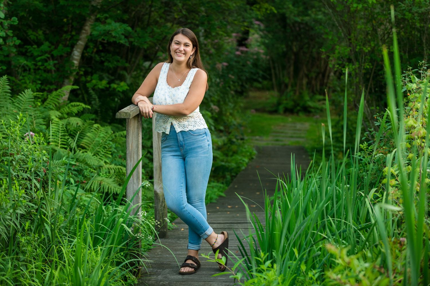 Woman walking along a lush garden path with tall green grasses.