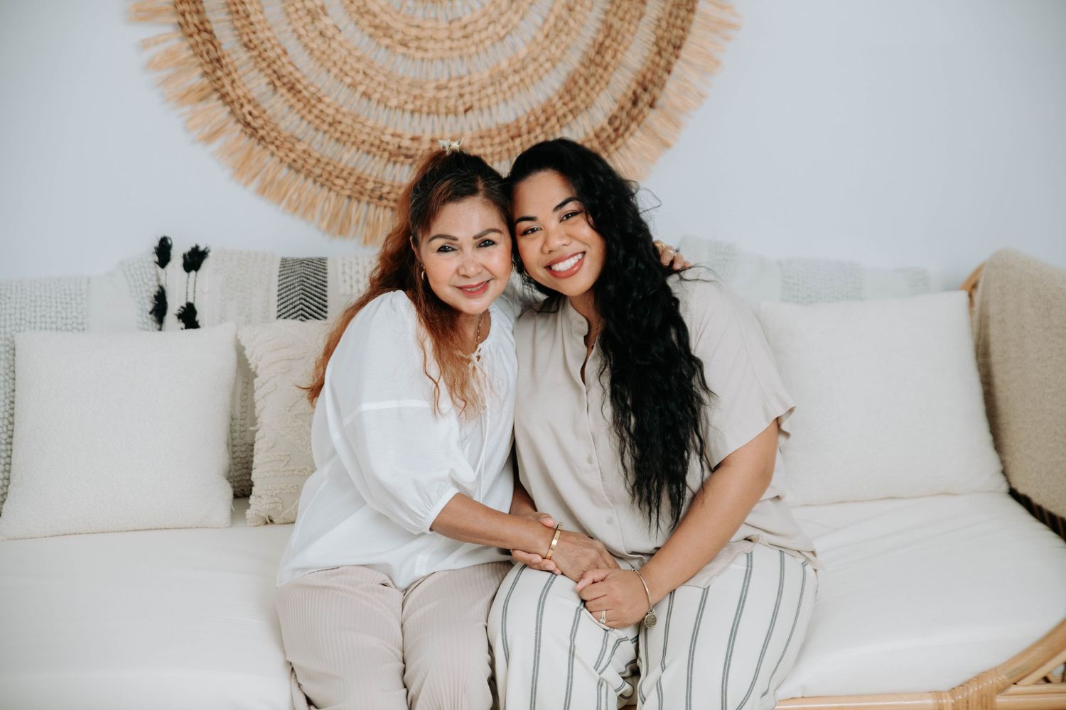 Two people share a joyful moment on a couch with a woven circular wall hanging behind them.