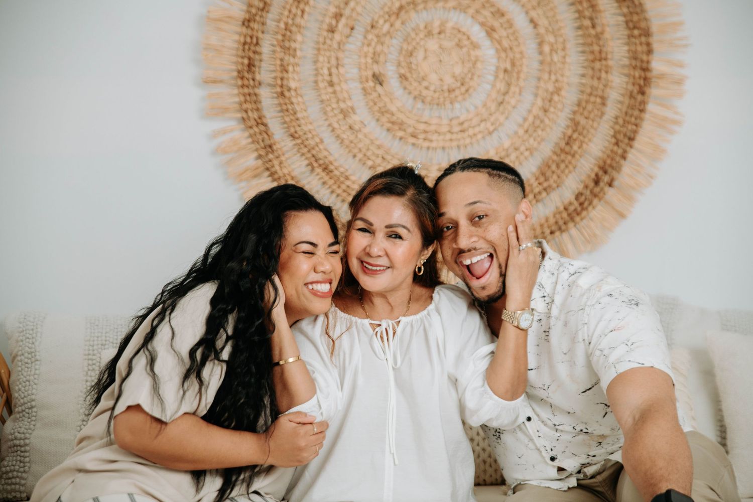 Three people pose playfully on a white couch against a beige circular wall decoration.