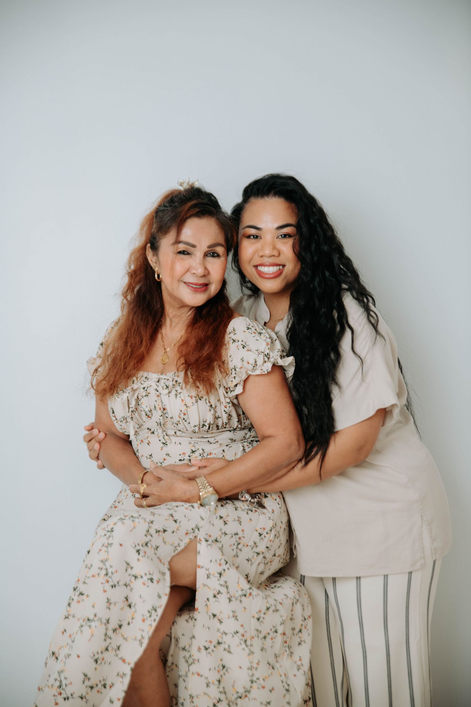 Two people in floral and neutral outfits embrace while posing against a white background.