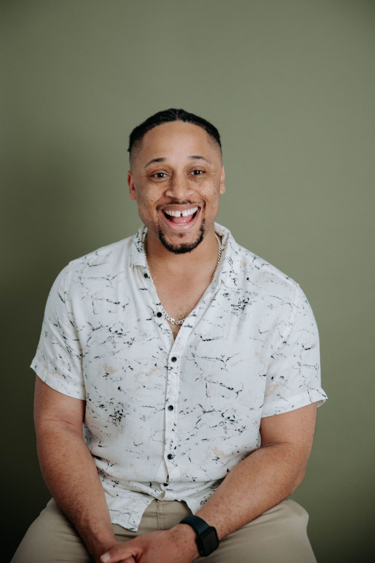Portrait of someone in a white patterned shirt smiling against a green background.