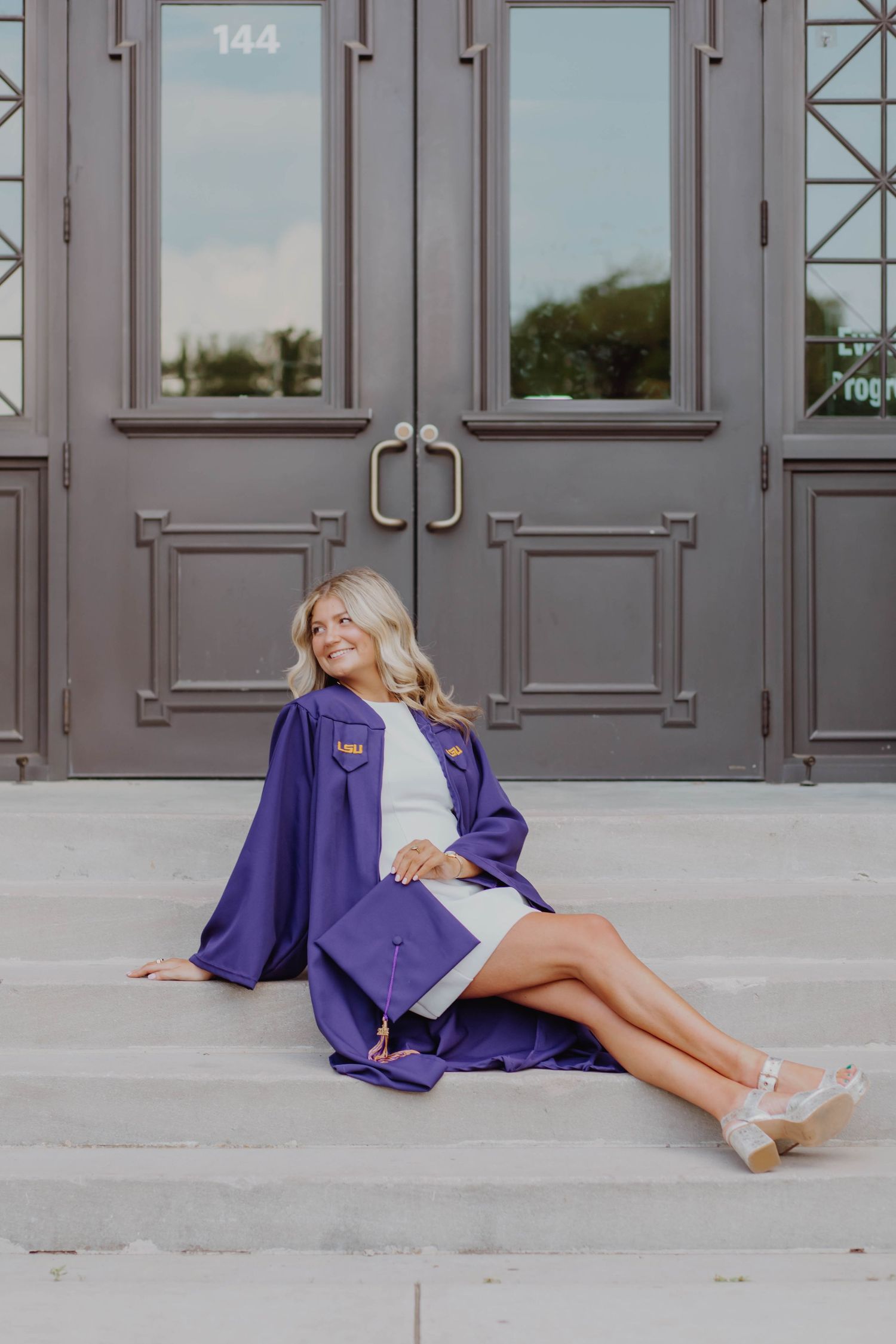Graduate in purple gown poses on steps in front of gray doors.