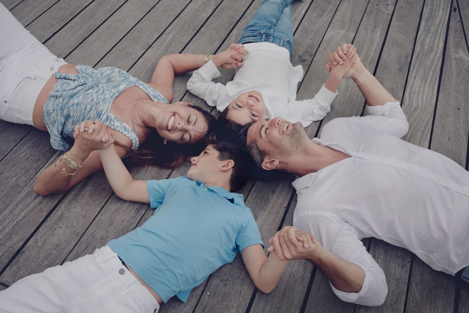 Family of four lying together on wooden deck floor with their heads forming a circle.