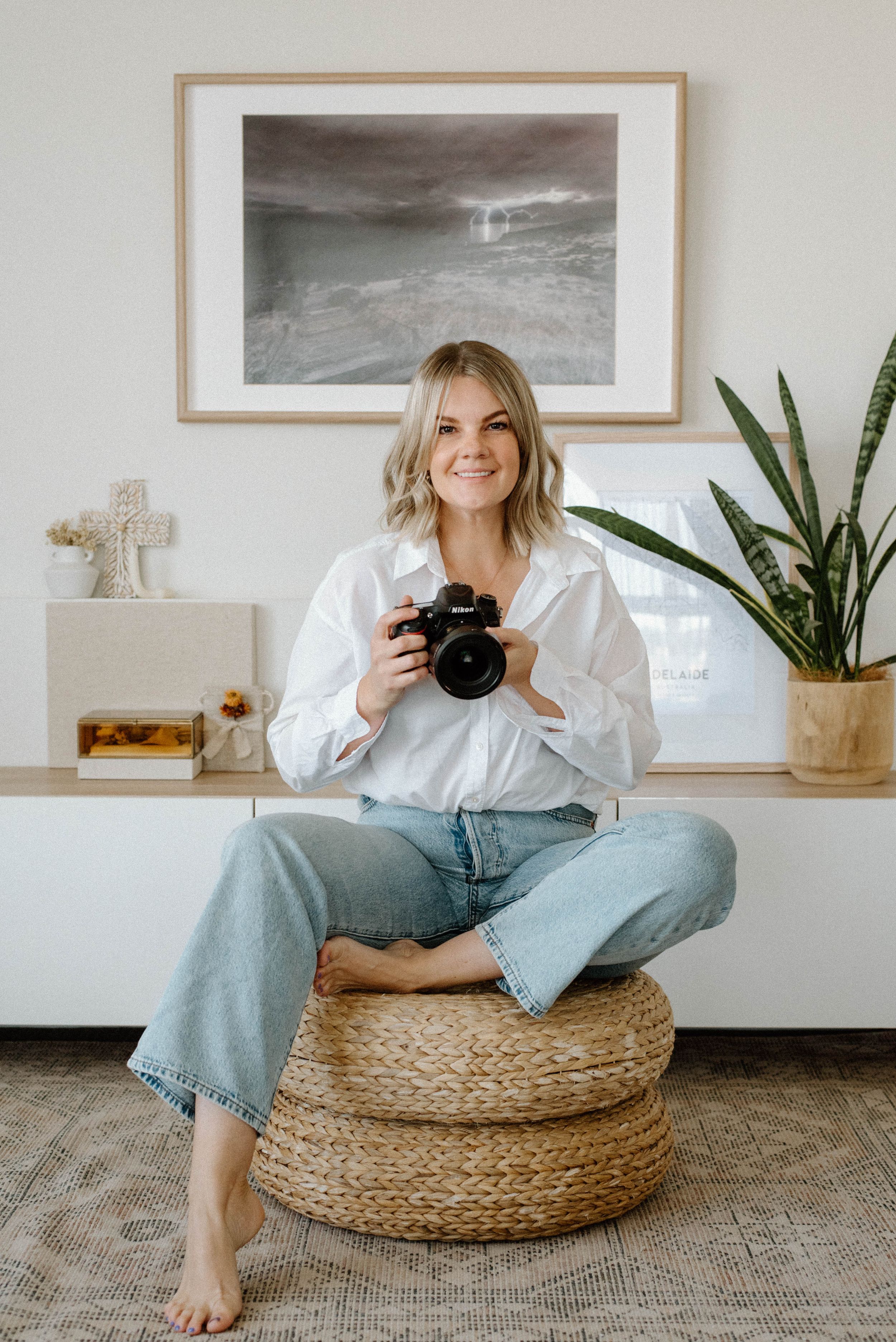 Photographer sitting cross-legged on woven poufs with camera in minimal white room.
