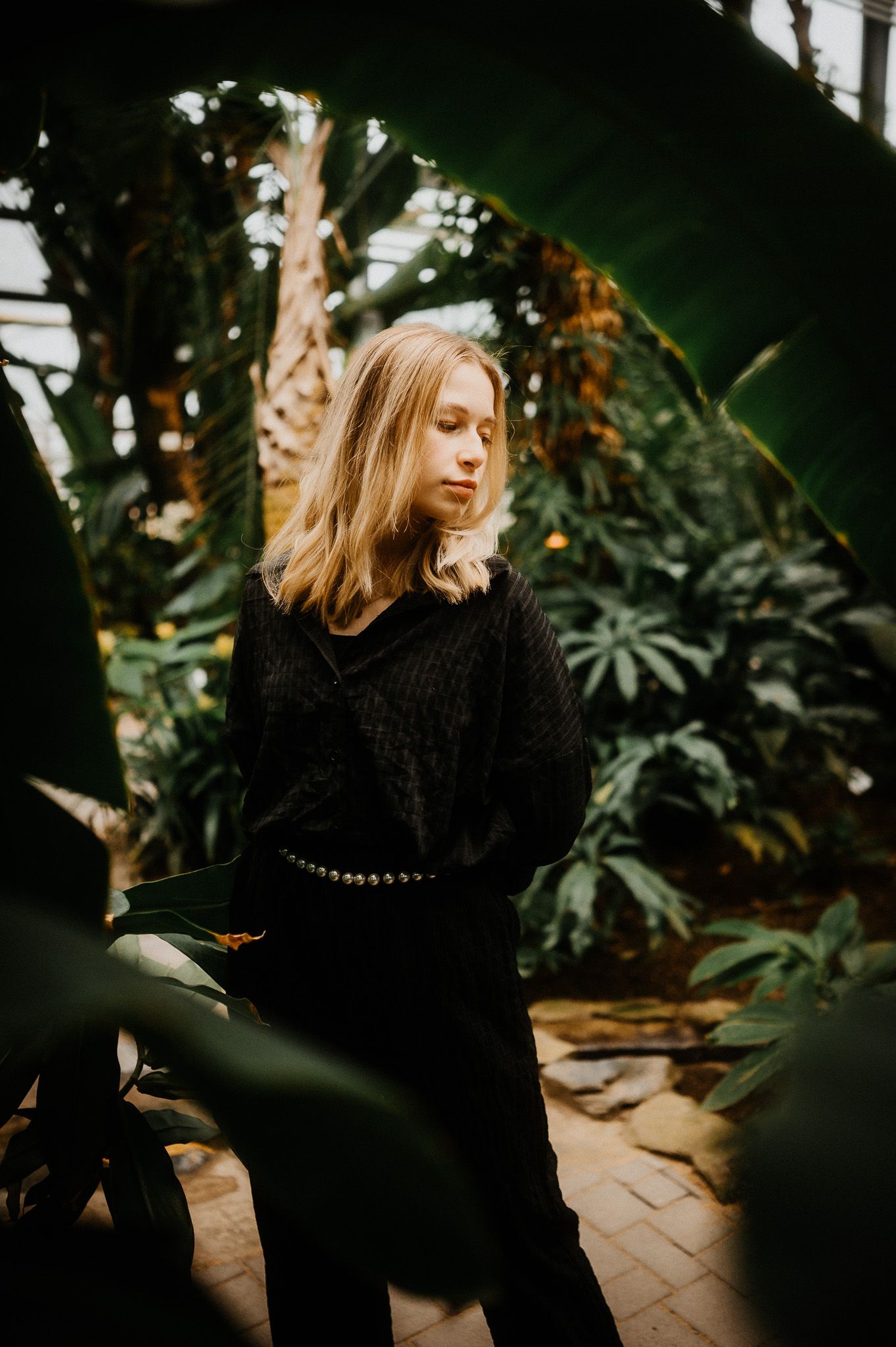 Artistic portrait in a greenhouse with lush tropical plants and moody lighting.