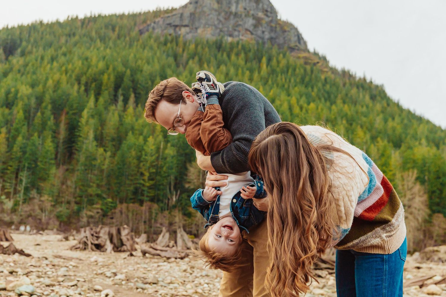 Playful family moment captured against mountain backdrop with evergreen forest.