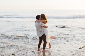 A romantic embrace on a beach at sunset with gentle waves rolling in the background.