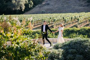 A romantic couple walks through lush vineyard rows on a sunny afternoon at a countryside winery estate.