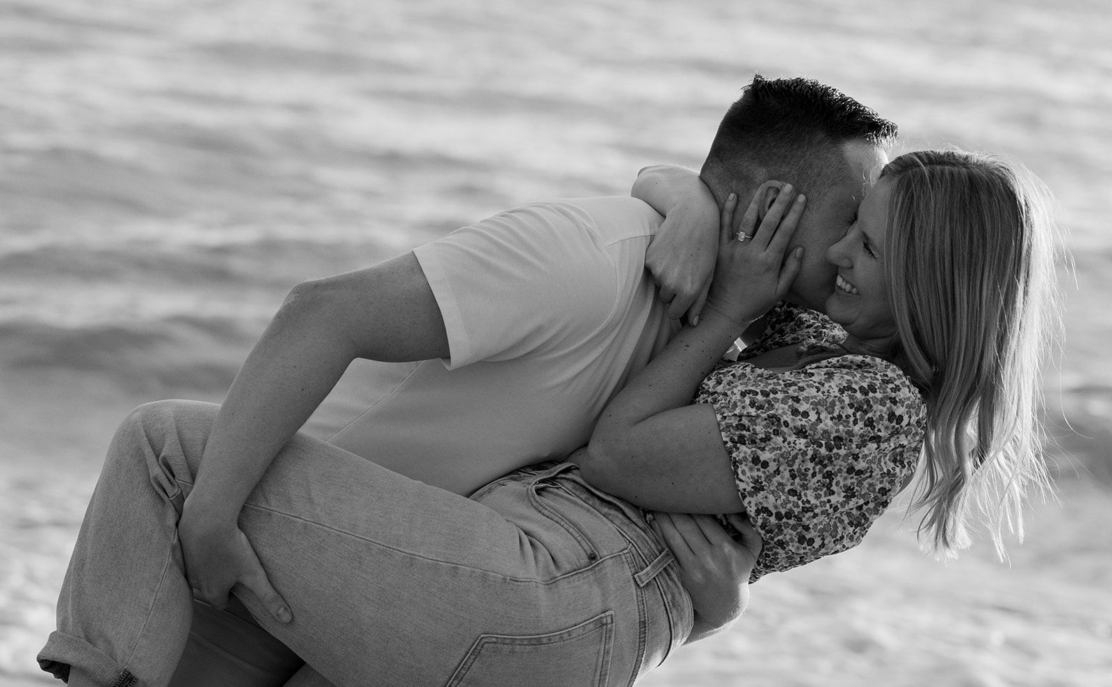 A black and white montage showing multiple romantic beach scenes of a couple kissing by the ocean waves.
