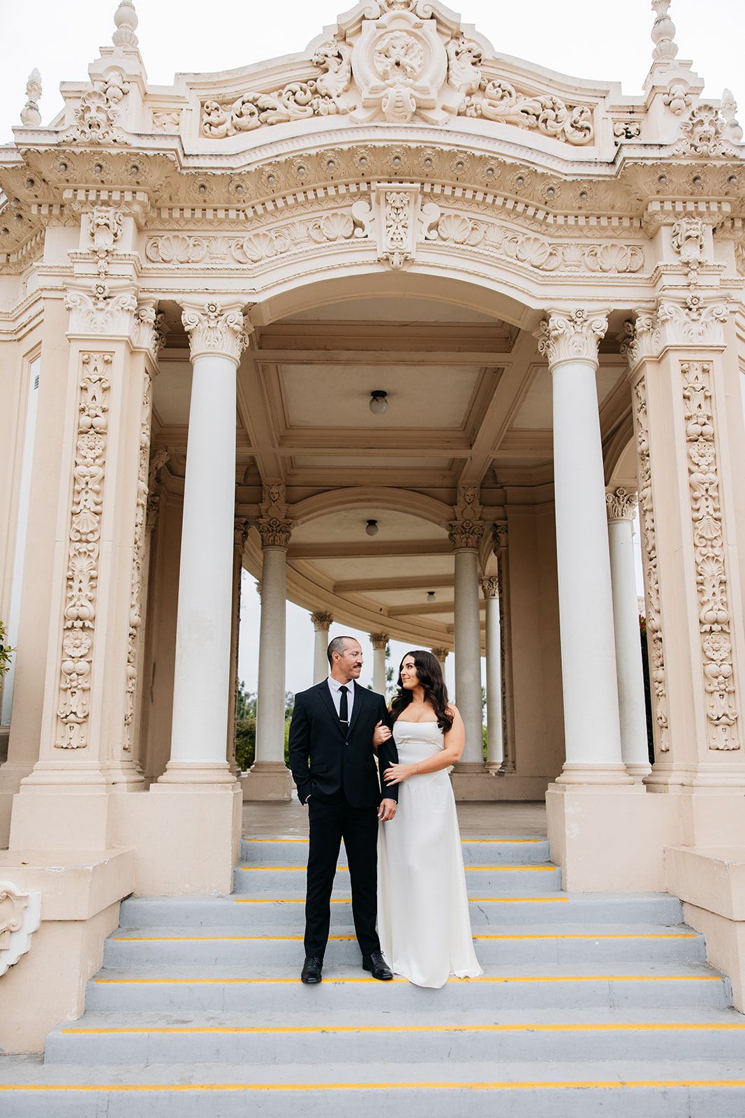 Couple take romantic photos at ornate white colonnade with elegant architectural details and blue striped steps.