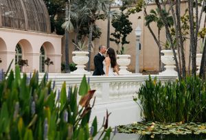 Artistic wedding photography captures a couple walking through a Mediterranean-style courtyard with tropical landscaping.