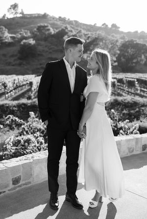 Newlywed couple sharing romantic moments outdoors on a garden terrace overlooking scenic hills in black and white.