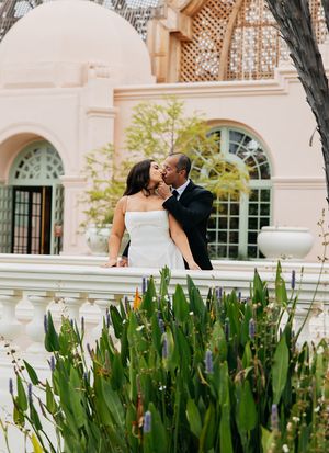A couple poses for wedding photos in front of an elegant building with lattice windows and green plants.