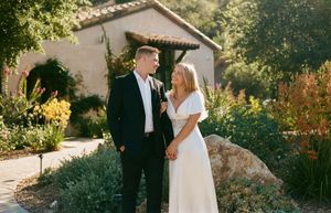 A sunlit wedding photoshoot with a couple standing among Mediterranean landscaping and Spanish architecture.